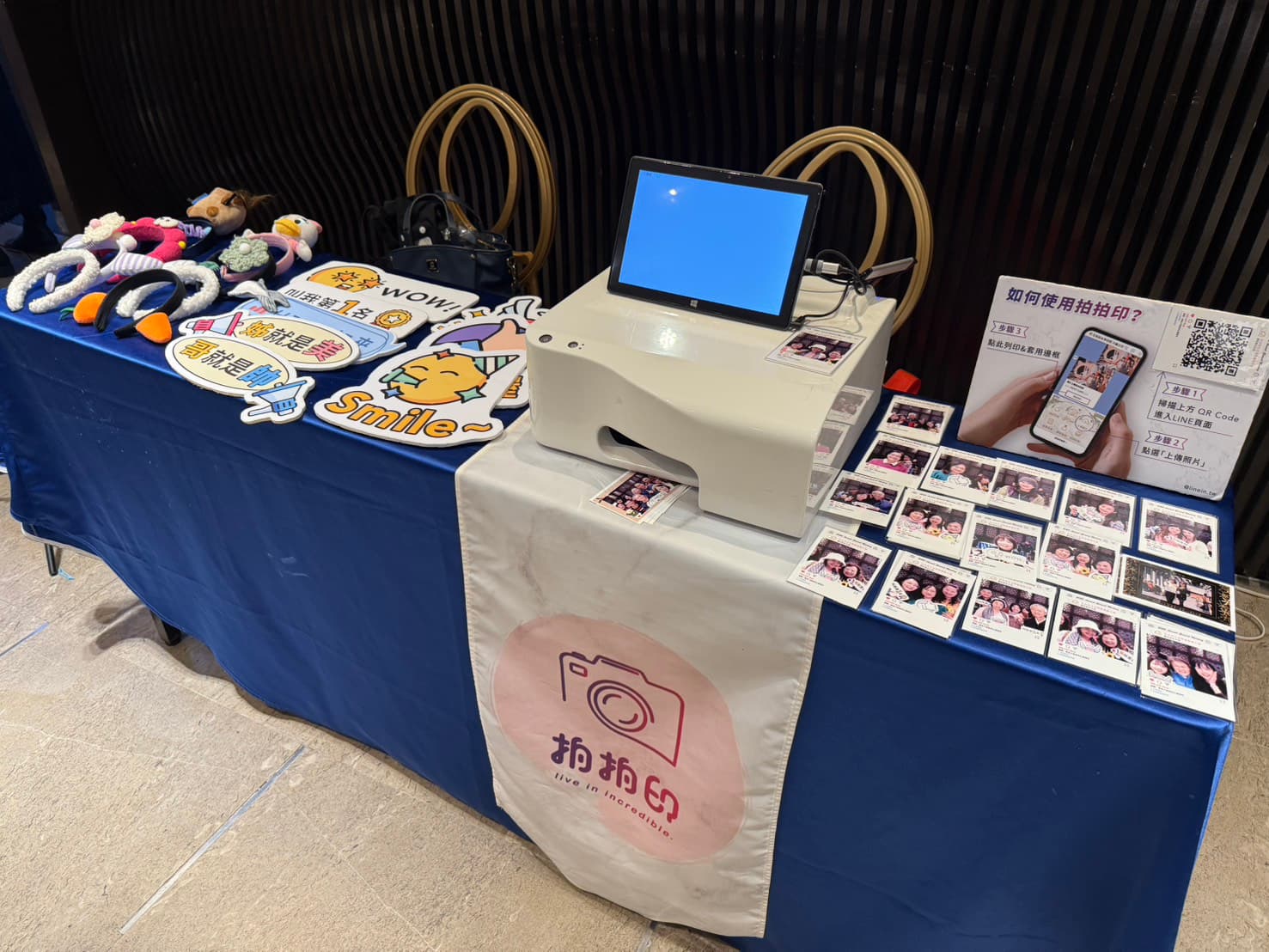 A draped table holding a photo printer, a tablet, props and a spread of freshly printed photos