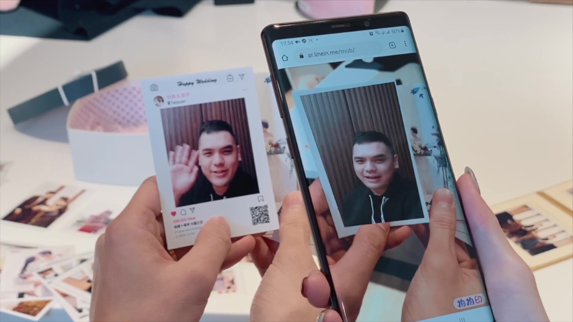 Static print in the left hand, the same photo moving on the phone in the right hand