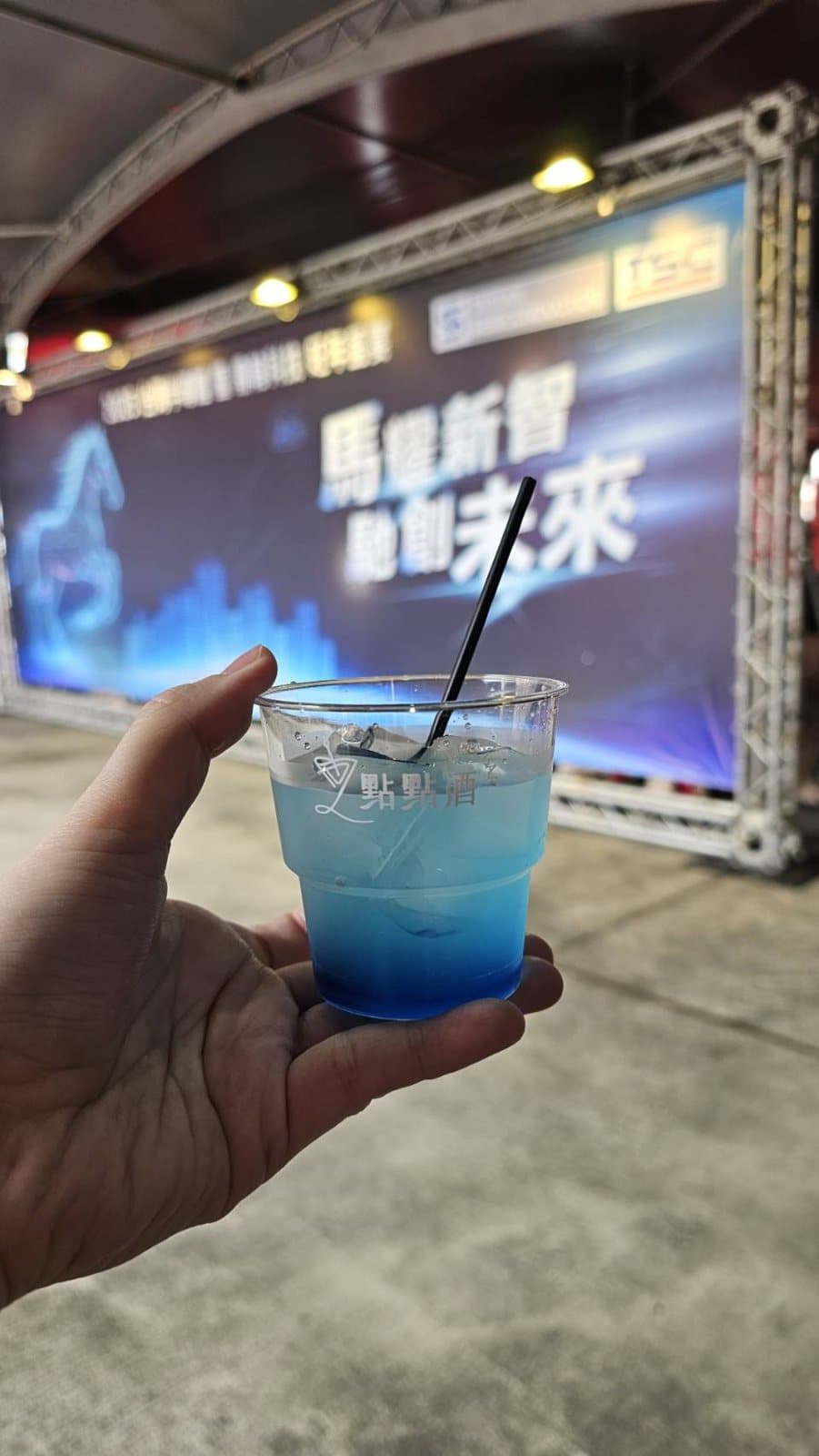 A guest holding a blue gradient cocktail facing the stage