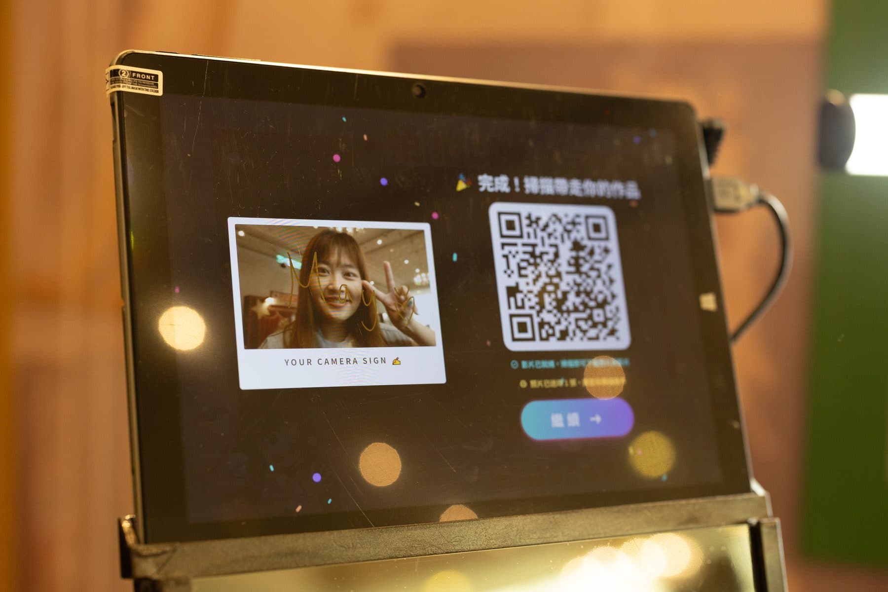 The booth screen showing a finished piece — signature composited over the photo, QR code for collection at right