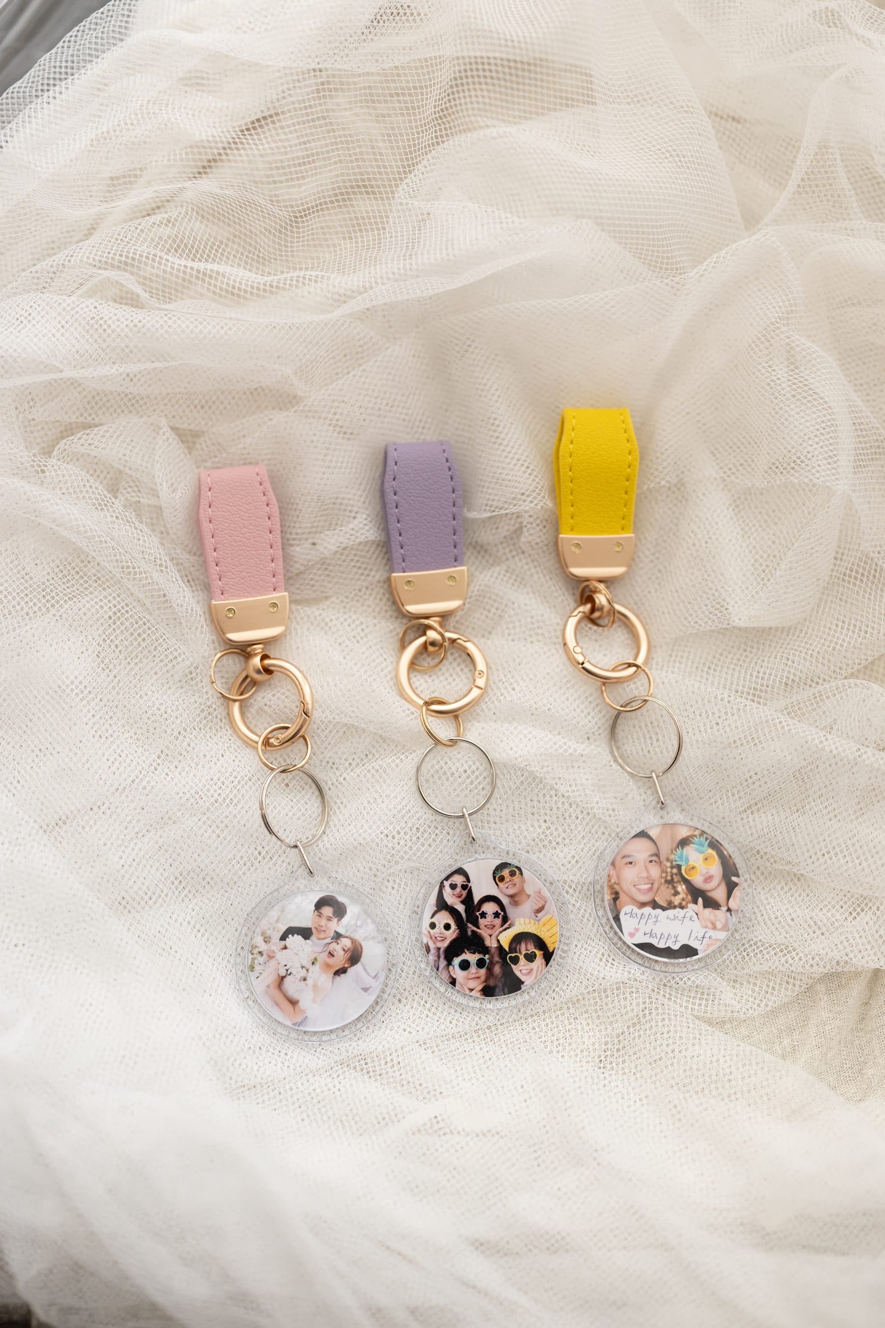 Three round acrylic keyrings side by side with pink, purple and yellow leather straps and different photos