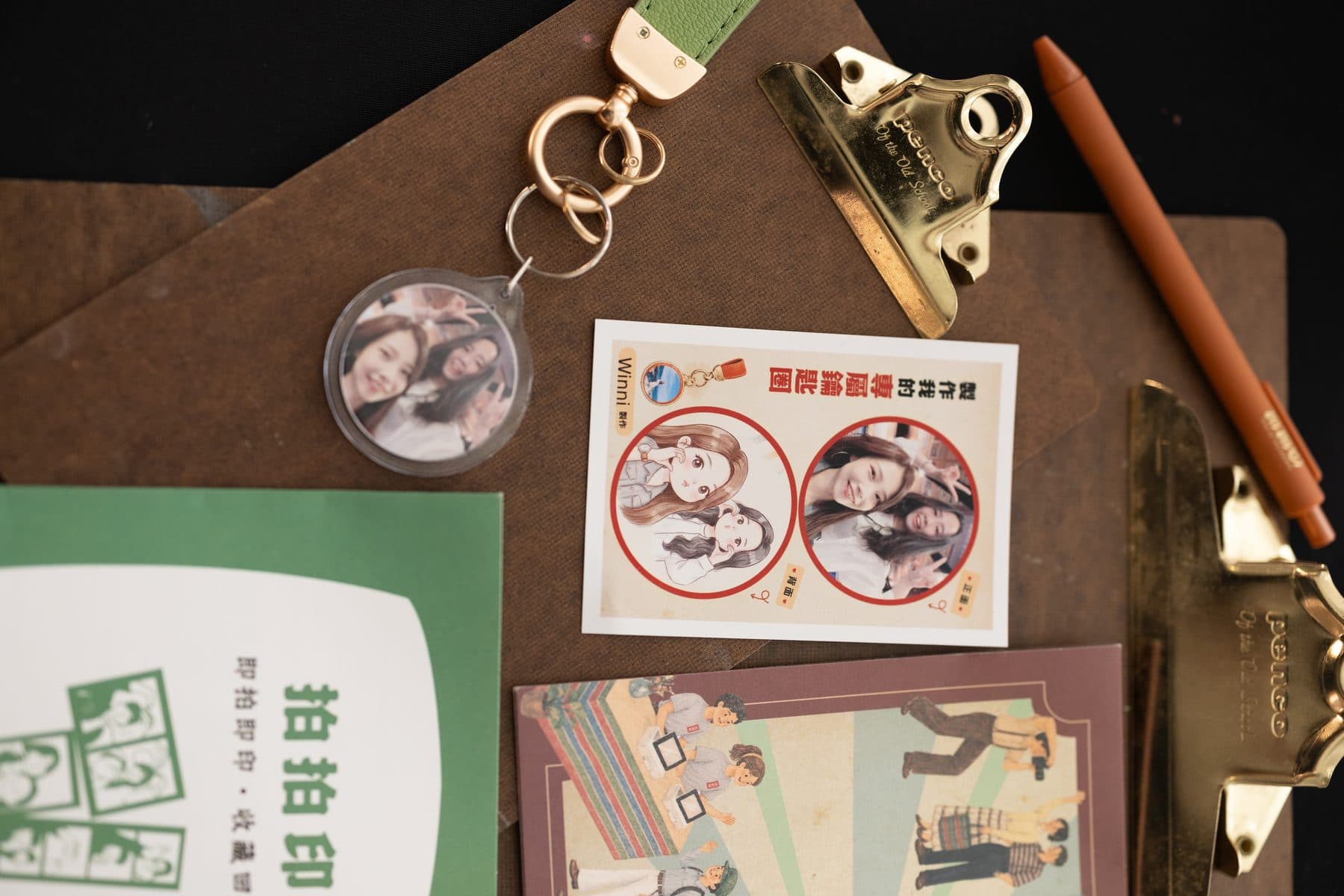 A finished keyring on a desk beside stickers printed with the same photo and an event leaflet