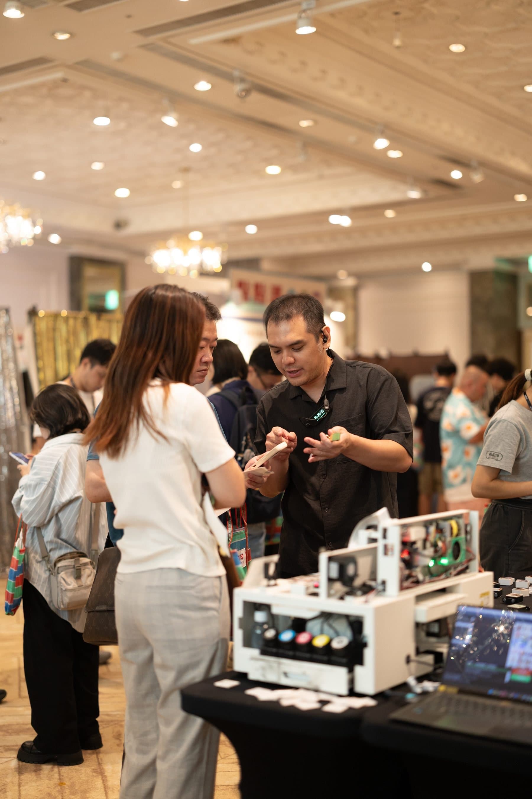A crew member explaining the UV printer to guests, with freshly printed panels on the table