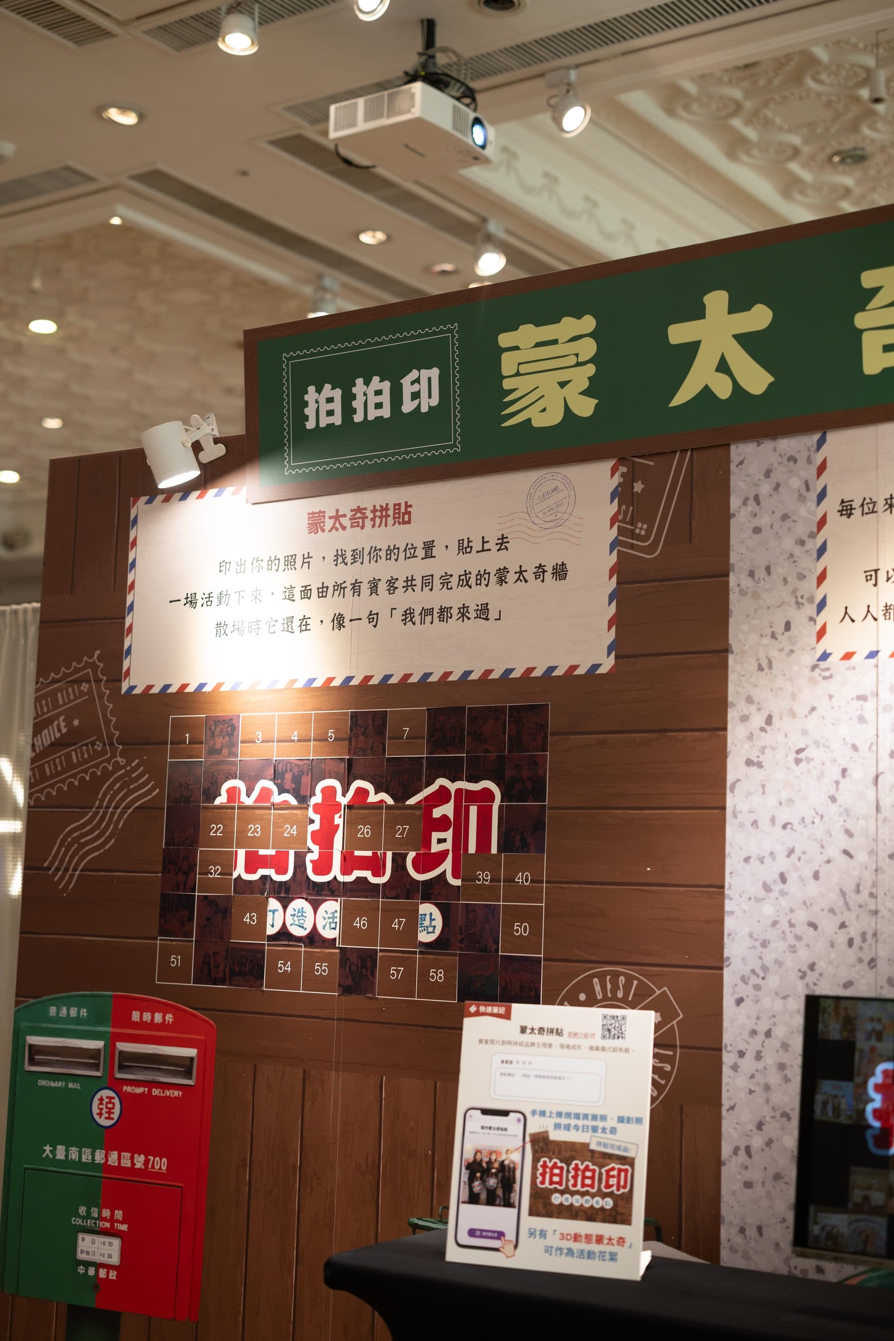 A photo mosaic wall on wood where guest photos tile into the brand wordmark, with a postbox prop and instruction board