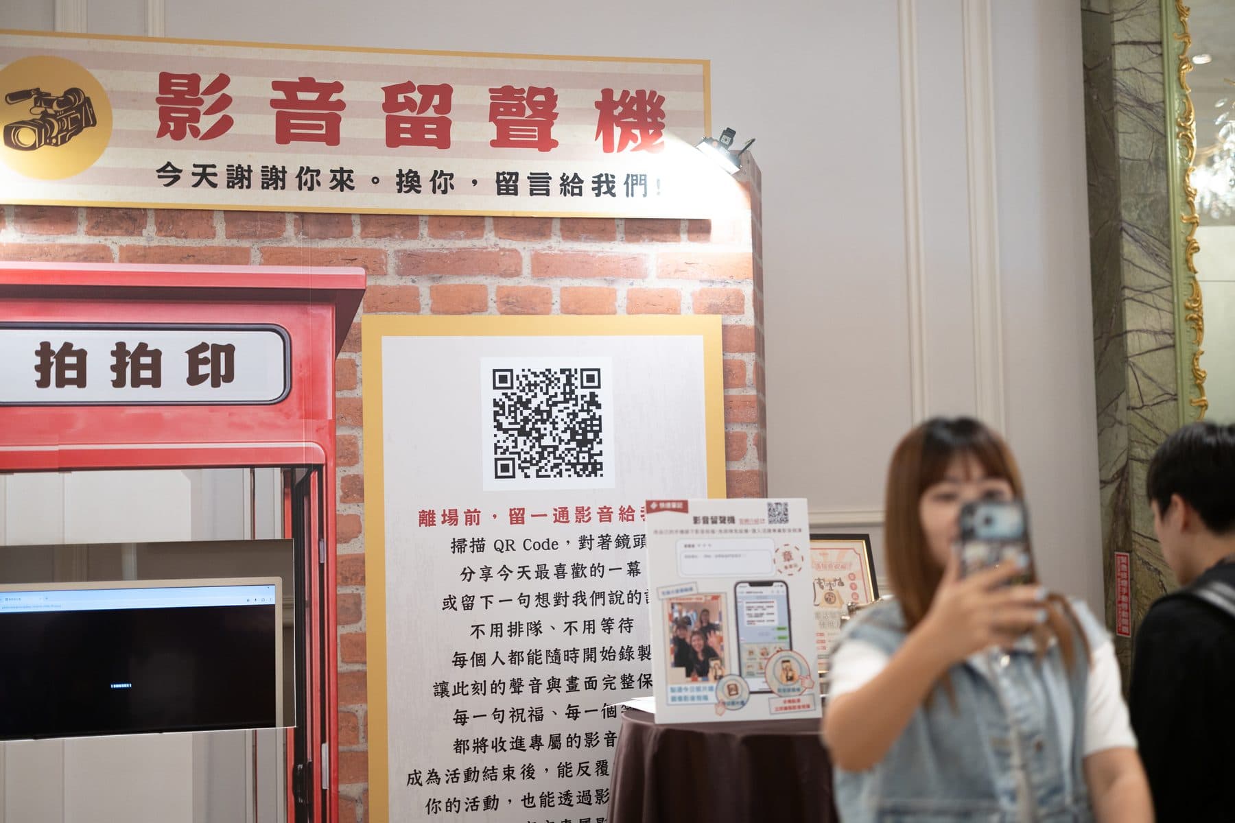The video guestbook stand — a red vintage phone-booth structure with a QR code and instructions