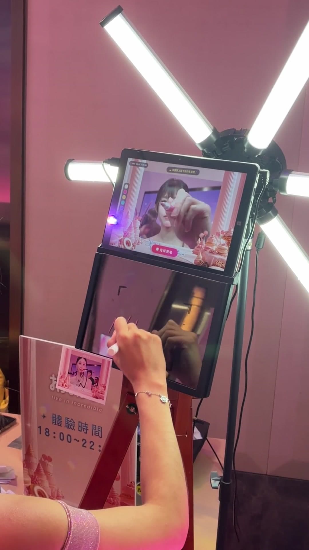 Camera sign booth on site: the top screen mirrors the guest live while she signs on the lower mirror with the stylus, strokes appearing in sync, light bars either side