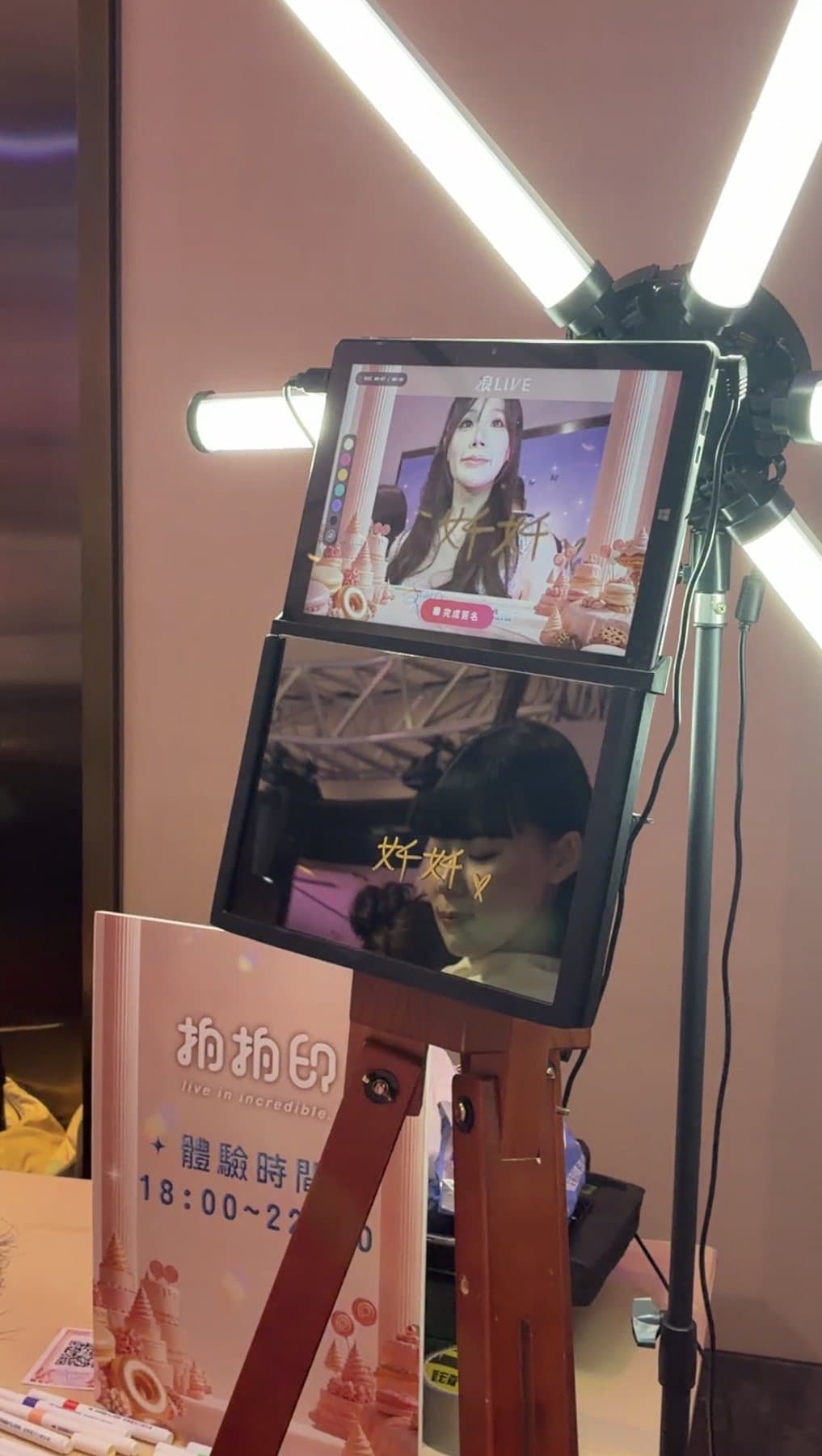 The booth’s top screen showing the guest live, with a freshly printed signed photo card hanging in front