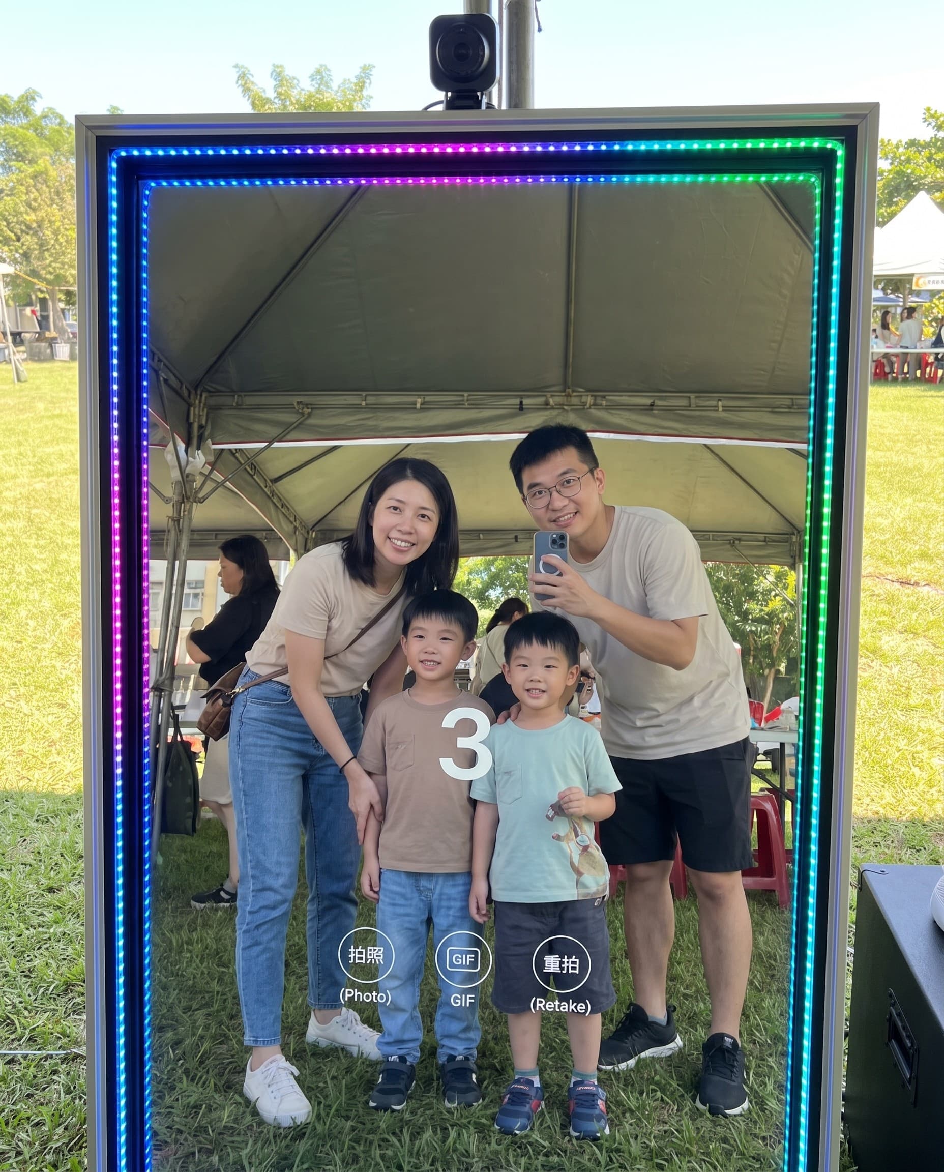 A family at the magic mirror at an outdoor family day, kids making faces