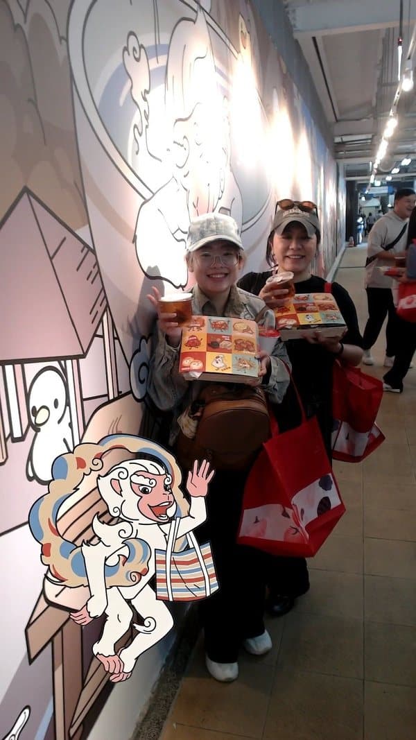 Photo with mascot booth — guests walking in frame with an illustrated monkey mascot at an outdoor food market event