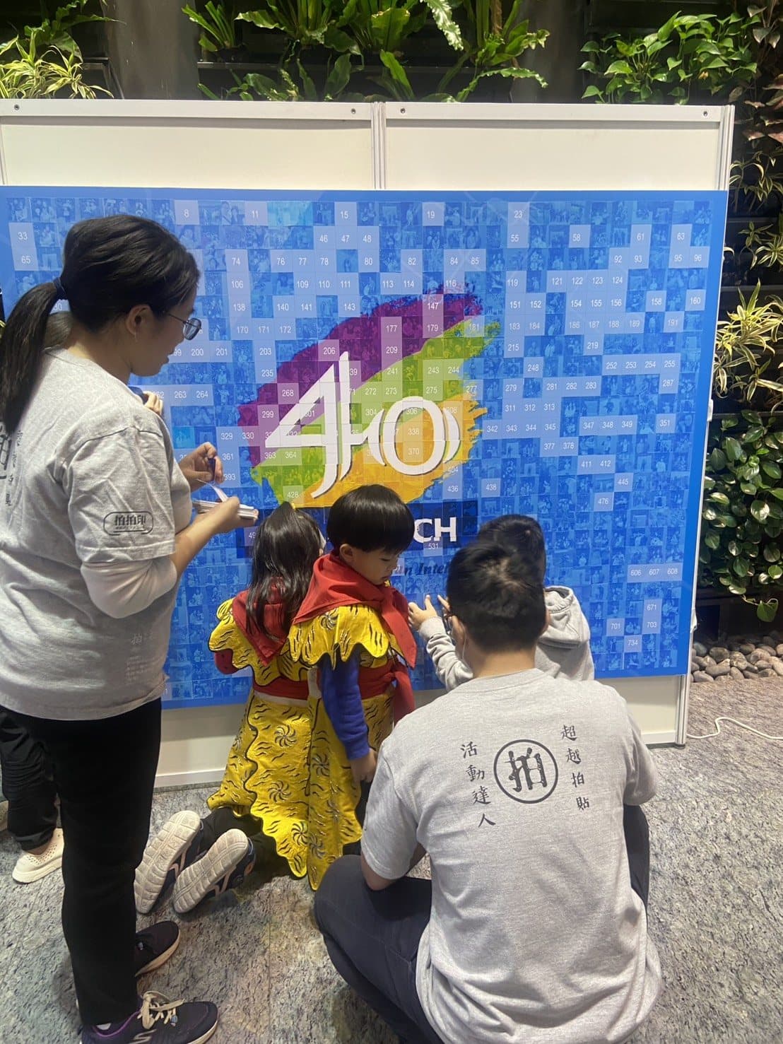 Guests place their photos onto a "40" anniversary mosaic wall at a tech company family day