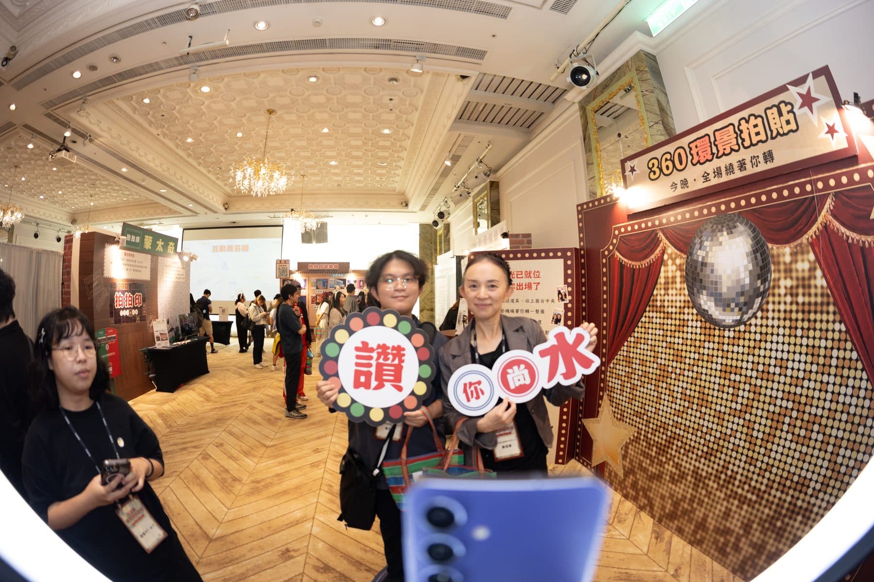 Two guests holding custom prop signs in front of the 360 booth backdrop