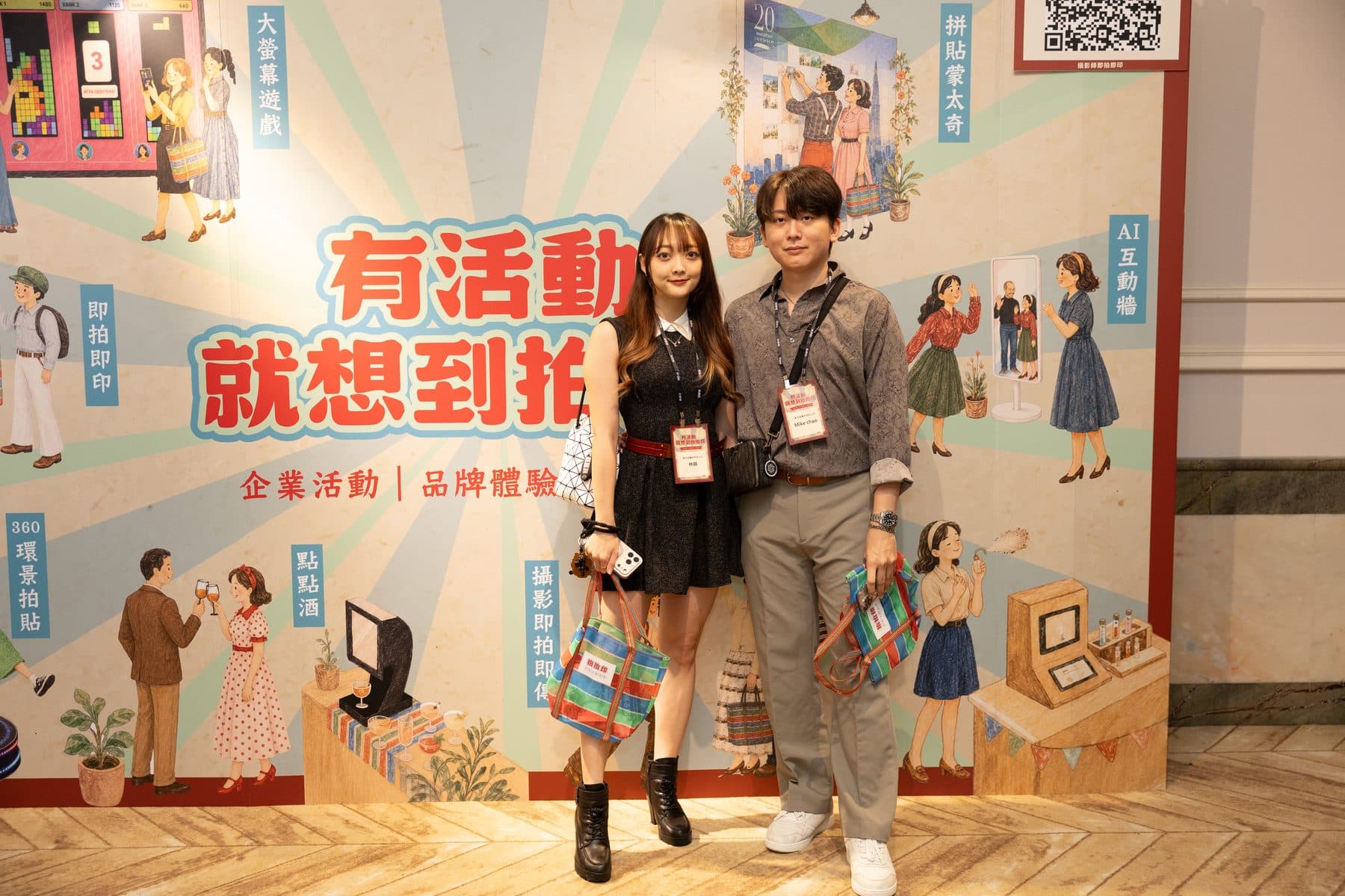 Two guests wearing on-site printed badges in front of the main backdrop