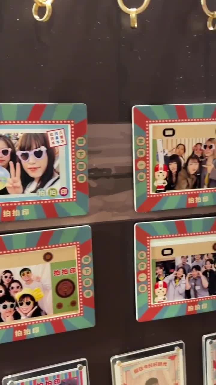 The camera tracks along a wall of magnetic photo frames, each holding a different guest’s print