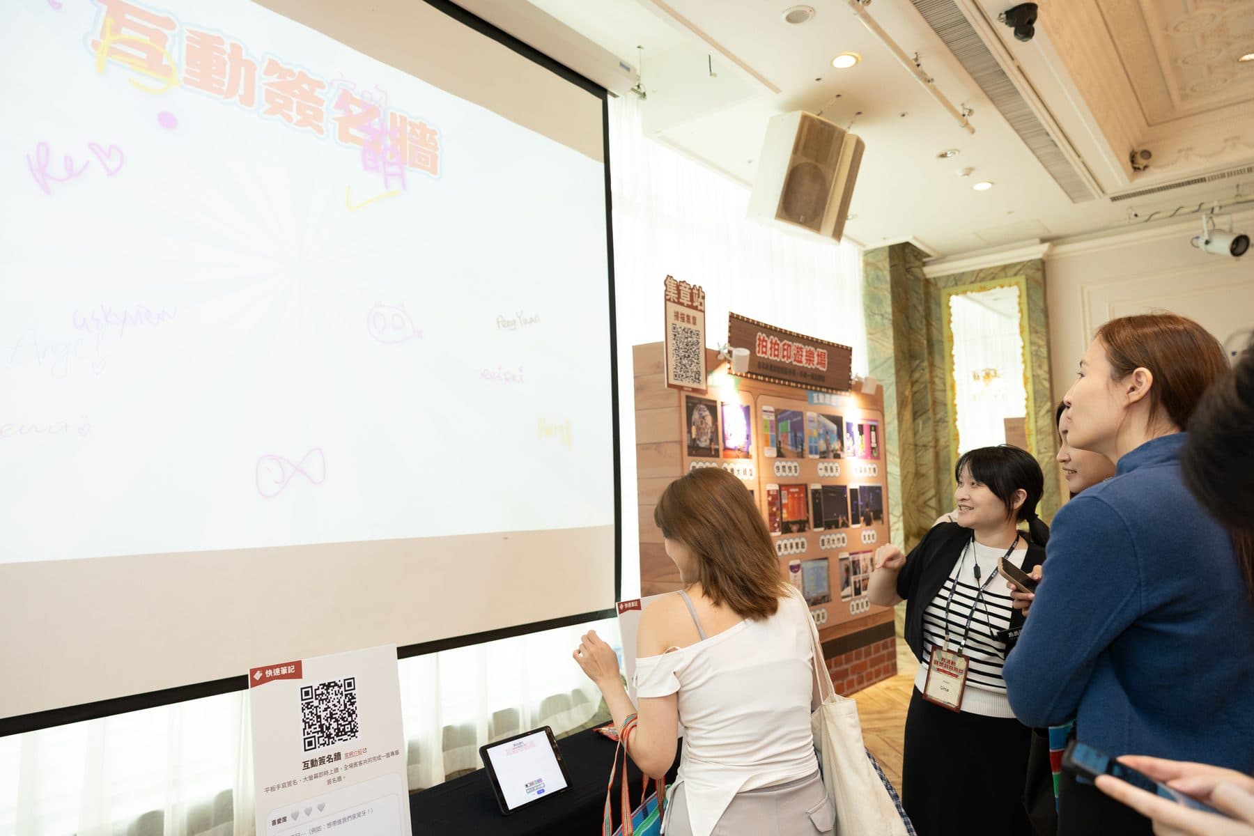The signature wall projected on the venue screen, filled with handwritten signatures, guests watching