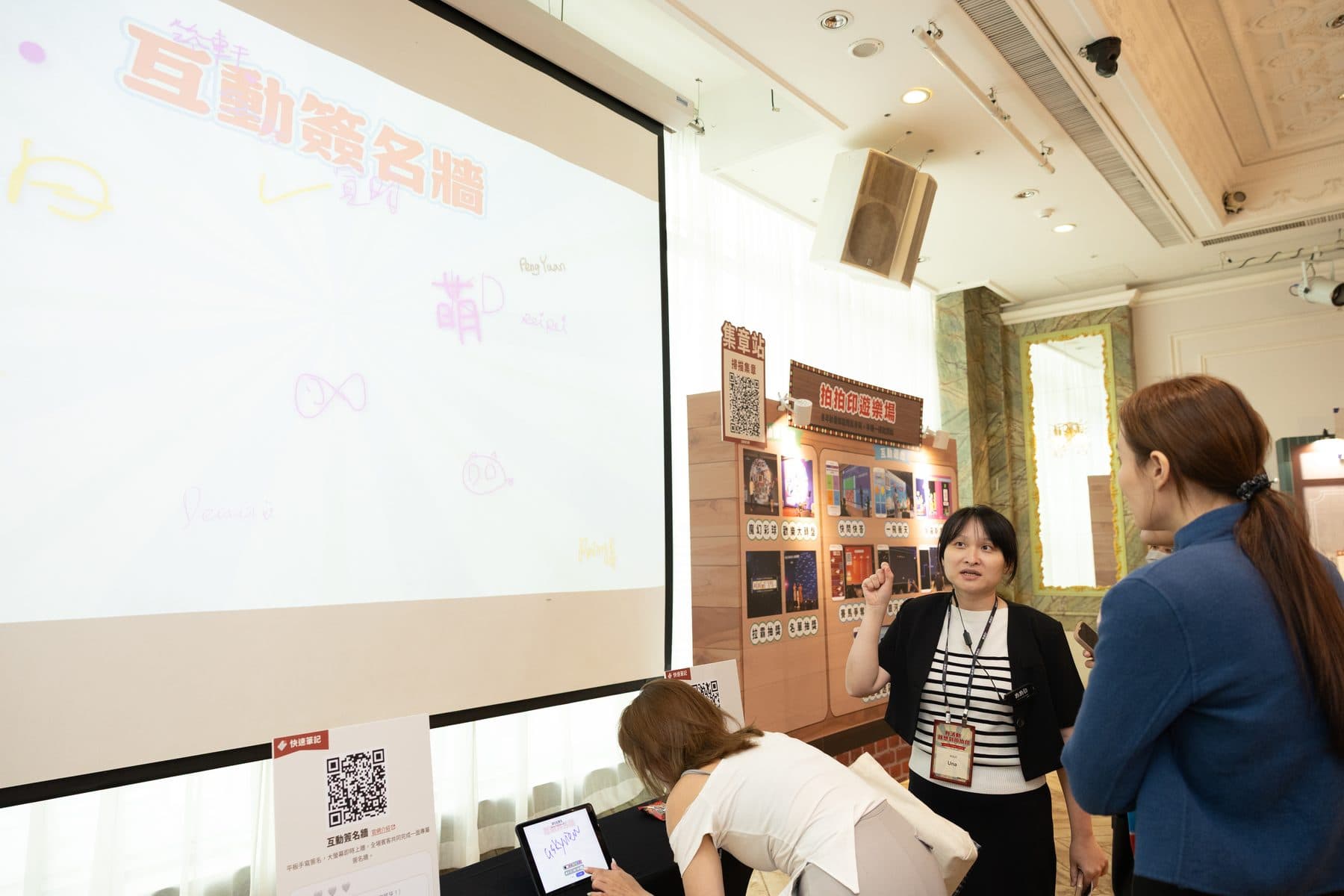 A crew member introducing the signature wall beside the projection screen, already carrying many signatures